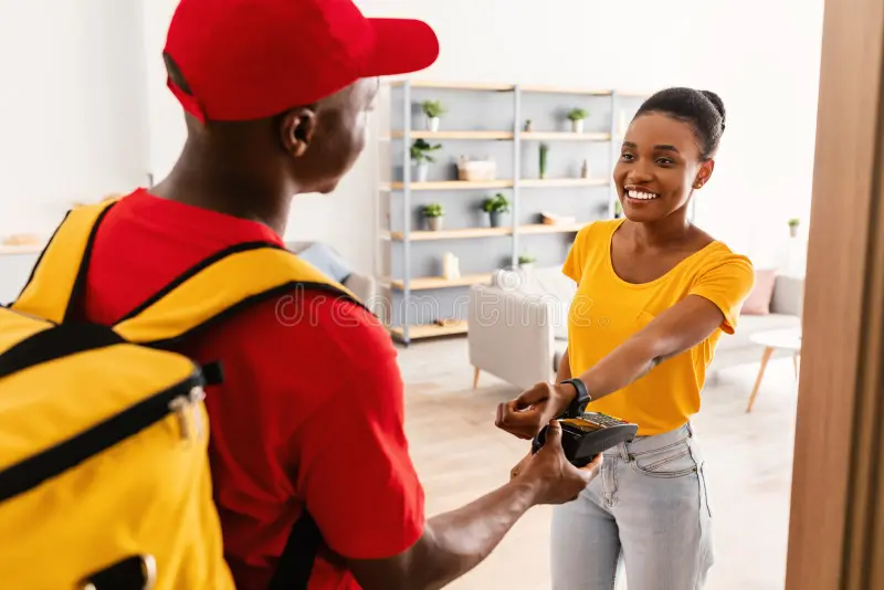 afro-américaine-payant-le-livreur-avec-smartwatch-à-la-maison-afrique-mettre-montre-au-paiement-terminal-faire-pour-livraison-de-228653701.webp